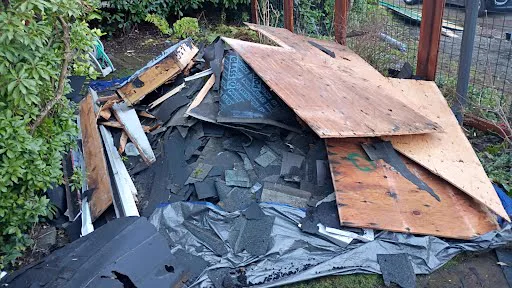 Pile of torn-off roofing shingles, plywood, and underlayment