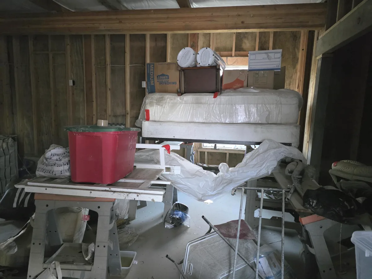 Outbuilding filled with a mattress, bins, and household items before a cleanout