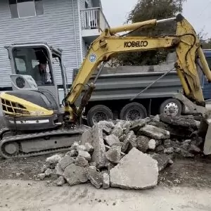 Mini excavator loading broken concrete into a dump truck