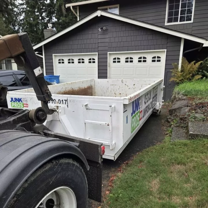 Roll-off truck setting a dumpster down in a residential driveway